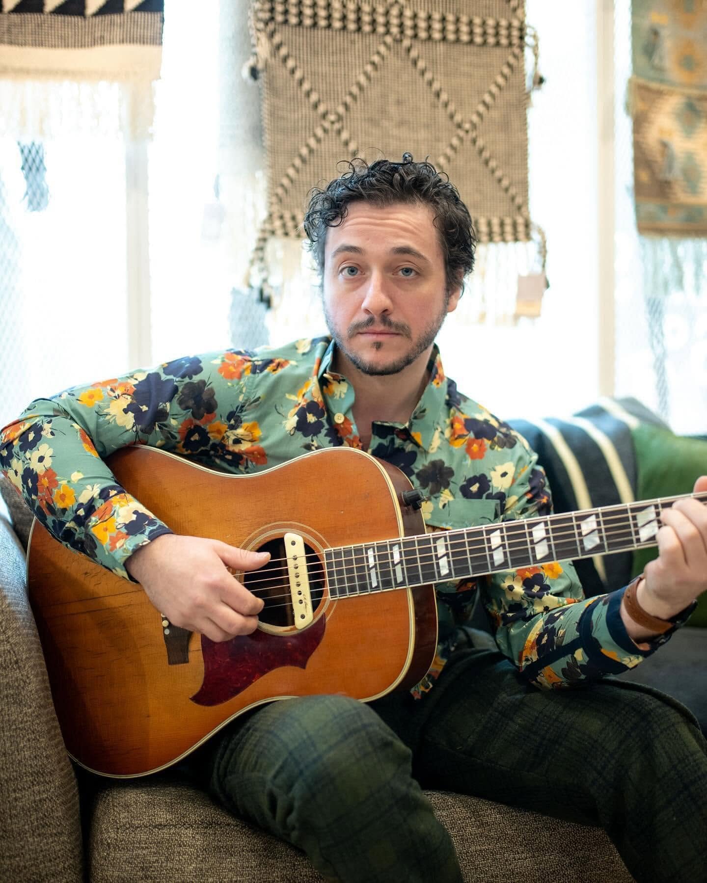 Nathan sitting with an acoustic guitar in a floral shirt
