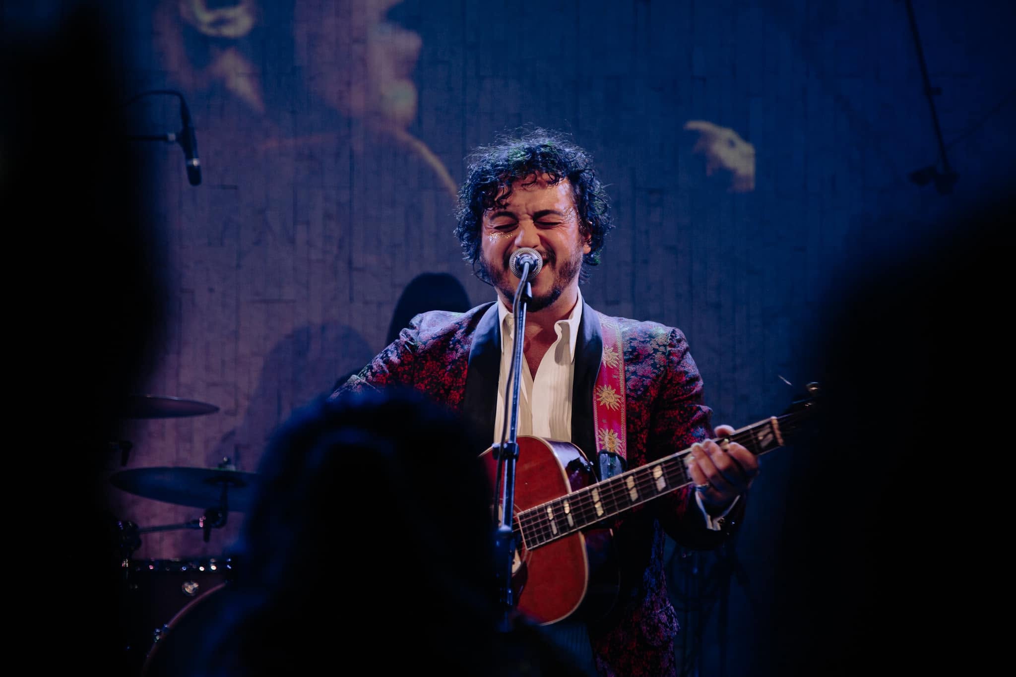 Nathan singing and playing guitar onstage in a patterned jacket